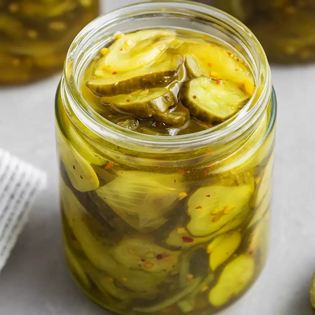 A jar of homemade bread and butter pickles with crinkle-cut cucumber slices, onions, and mustard seeds in a golden brine