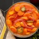 Colorful spicy pickled carrots with red onion and jalapeños in a glass jar, showing the diagonal-cut carrots covered in seasoned brine