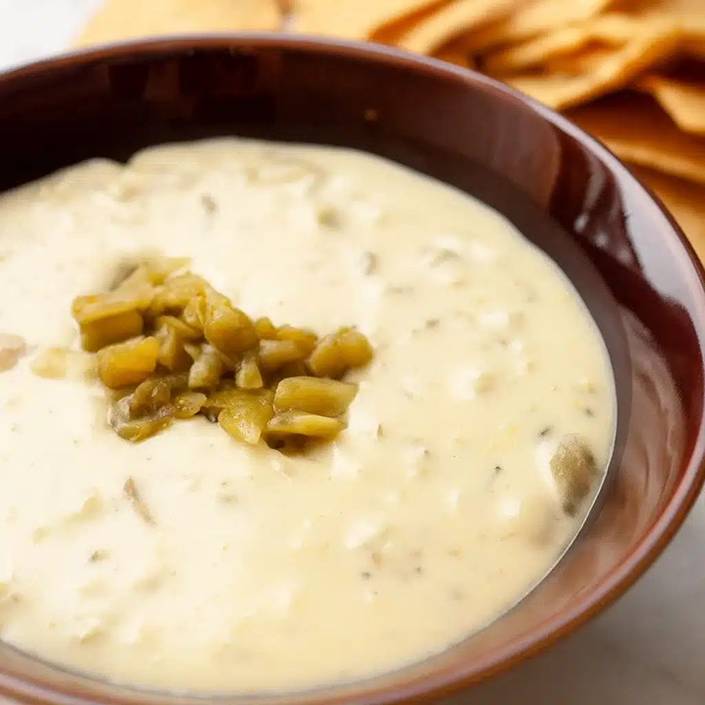 Creamy golden Hatch chile queso in a serving bowl surrounded by tortilla chips, garnished with fresh cilantro and diced green chiles