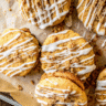 Golden brown pumpkin Coffee Cake cookies topped with buttery crumb topping and drizzled with white glaze, arranged on a cooling rack with fall leaves in the background.