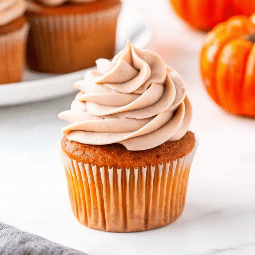 Perfectly frosted pumpkin spice cupcakes with cream cheese frosting, dusted with pumpkin pie spice, arranged on a rustic wooden board with fall leaves