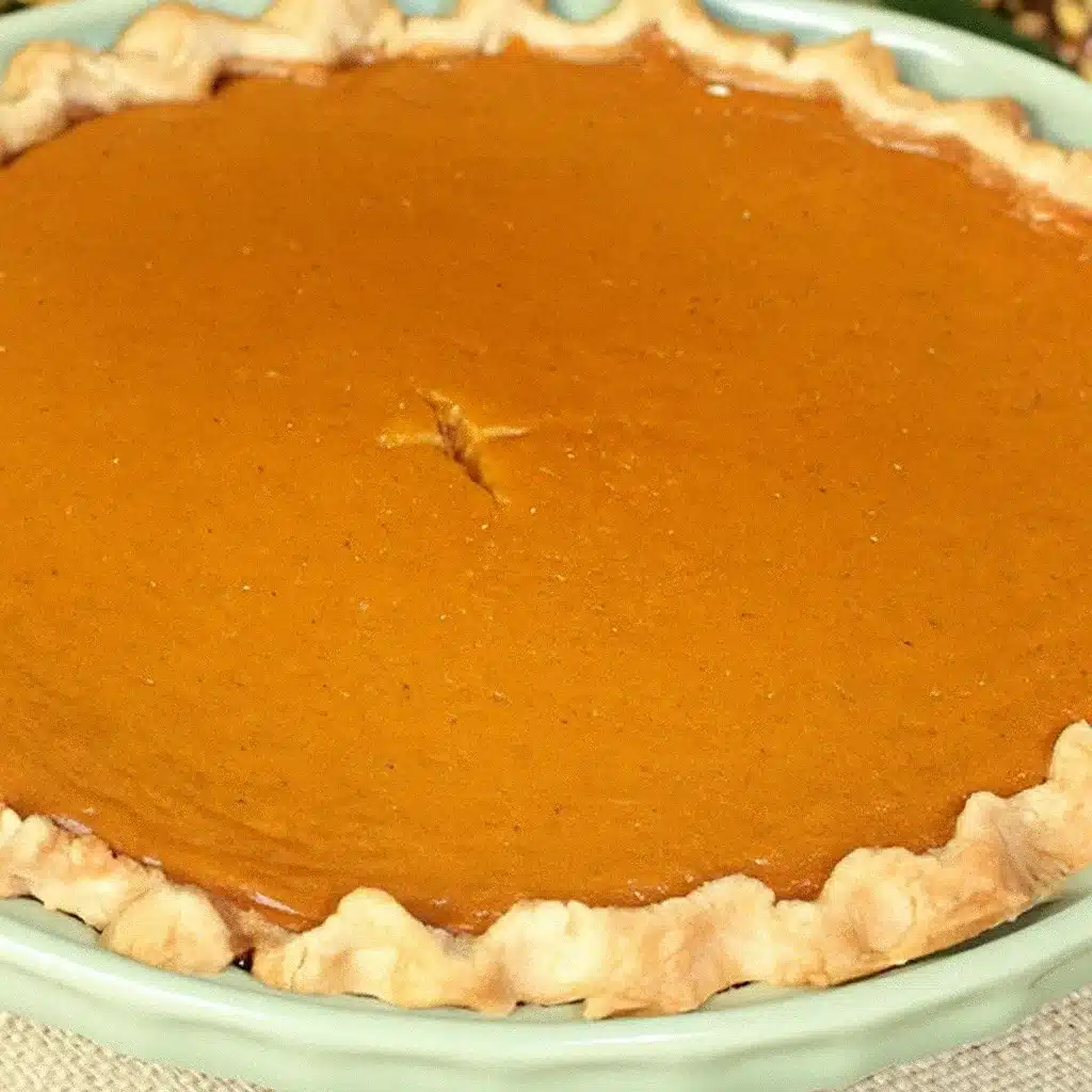 Golden brown pumpkin pie with flaky crust, garnished with sugared cranberries and whipped cream, served on a rustic wooden table with fall decorations