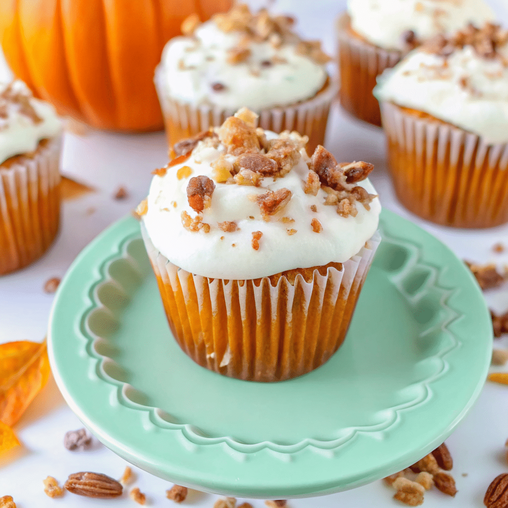 Golden pumpkin pecan cupcakes topped with swirled cinnamon cream cheese frosting and chopped pecans on a rustic wooden table with fall leaves