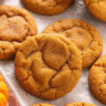 Soft, chewy vegan pumpkin cookies with crackled tops arranged on a white plate, showing their perfect golden-brown color and tender texture